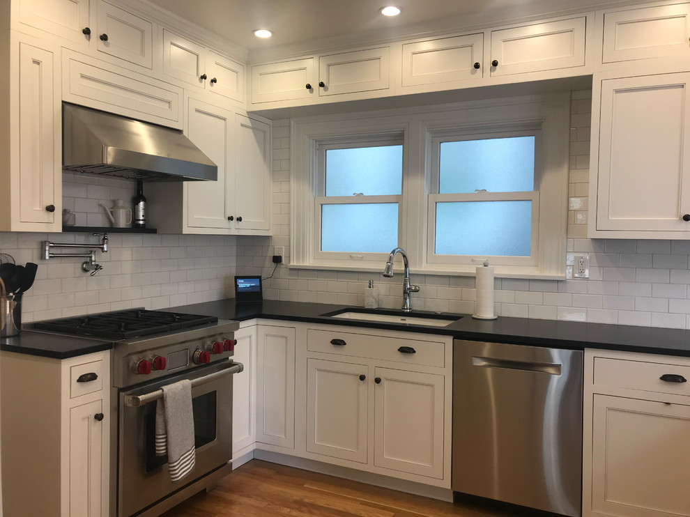 Enclosed kitchen - mid-sized traditional u-shaped medium tone wood floor enclosed kitchen idea in Seattle with an undermount sink, shaker cabinets, white cabinets, granite countertops, white backsplash, ceramic backsplash, stainless steel appliances, a peninsula and black countertops