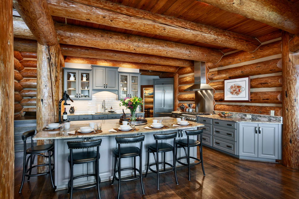 Rustik inredning av ett grå grått l-kök, med luckor med upphöjd panel, grå skåp, rostfria vitvaror, mörkt trägolv, en köksö och brunt golv