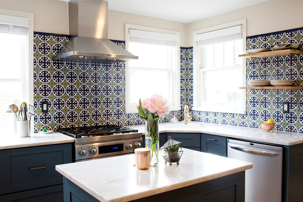 Cette photo montre une cuisine chic en L avec un placard à porte shaker, des portes de placard bleues, une crédence en céramique, une crédence multicolore, un électroménager en acier inoxydable et îlot.