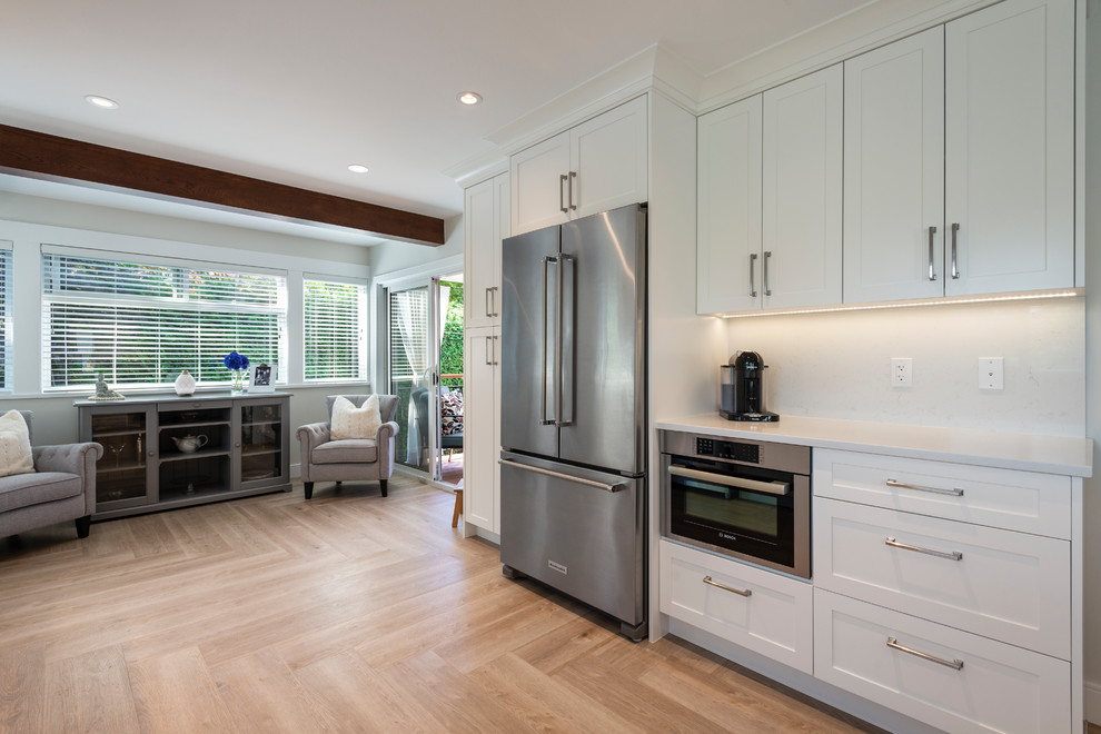 This is an example of a large contemporary l-shaped kitchen/diner in Vancouver with a belfast sink, shaker cabinets, white cabinets, quartz worktops, white splashback, stainless steel appliances, medium hardwood flooring, no island, brown floors and white worktops.