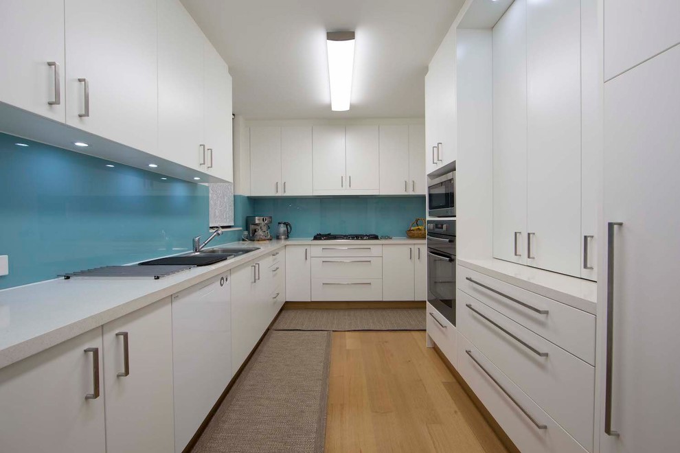 Design ideas for a medium sized contemporary galley kitchen pantry in Sydney with a built-in sink, flat-panel cabinets, white cabinets, engineered stone countertops, blue splashback, stainless steel appliances, medium hardwood flooring, no island and white worktops.