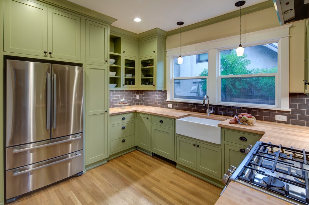 Amerikansk inredning av ett avskilt, mellanstort u-kök, med en rustik diskho, skåp i shakerstil, gröna skåp, träbänkskiva, blått stänkskydd, stänkskydd i keramik, rostfria vitvaror och ljust trägolv