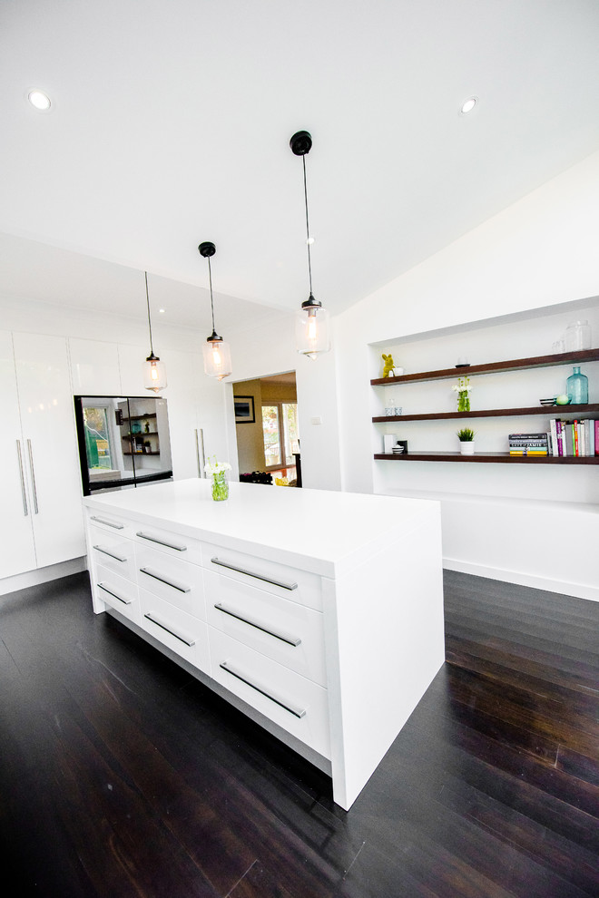 Photo of a medium sized contemporary l-shaped kitchen/diner in Sydney with flat-panel cabinets, white cabinets, engineered stone countertops, black splashback, an island, a submerged sink, porcelain splashback, stainless steel appliances, dark hardwood flooring, black floors and white worktops.