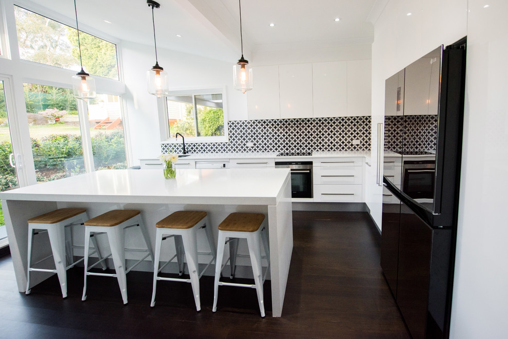 Mid-sized trendy l-shaped dark wood floor and black floor eat-in kitchen photo in Sydney with flat-panel cabinets, white cabinets, quartz countertops, black backsplash, an island, an undermount sink, porcelain backsplash, stainless steel appliances and white countertops