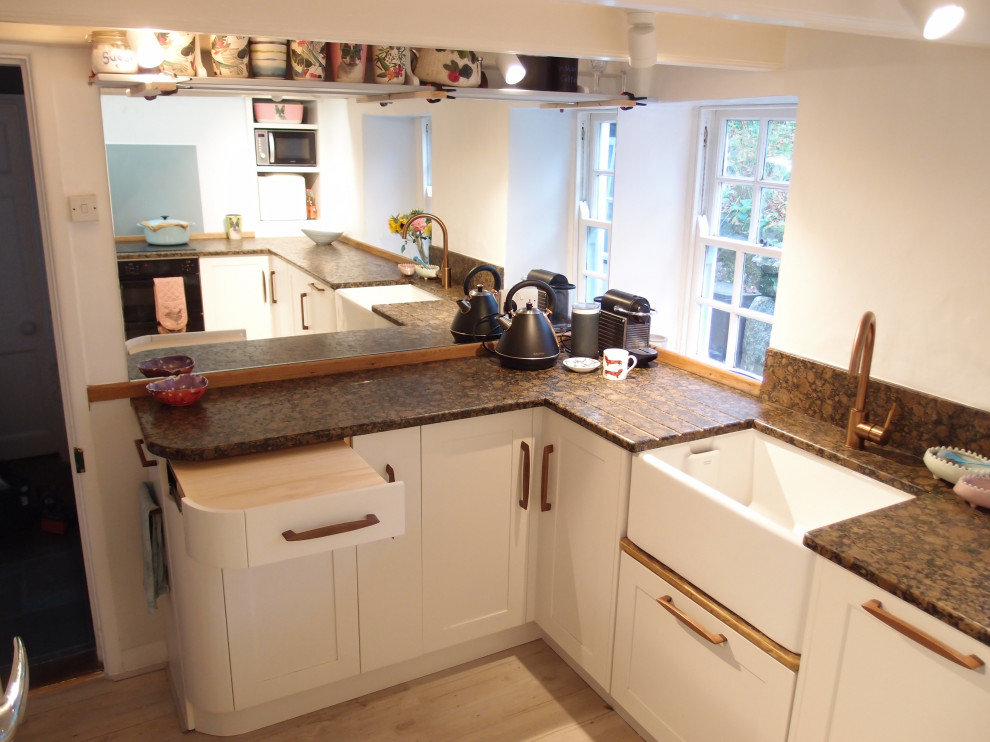 This is an example of a medium sized farmhouse u-shaped enclosed kitchen in Cornwall with a belfast sink, shaker cabinets, white cabinets, granite worktops, mirror splashback, black appliances, painted wood flooring, no island, white floors and brown worktops.