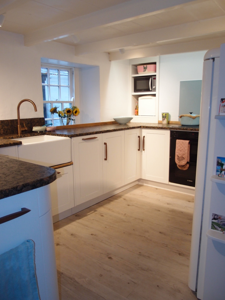 Inspiration for a medium sized country u-shaped enclosed kitchen in Cornwall with shaker cabinets, white cabinets, granite worktops, blue splashback, mirror splashback, black appliances, painted wood flooring, no island, white floors, brown worktops and a belfast sink.