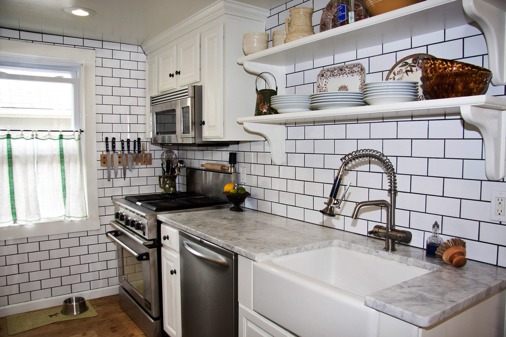 Small elegant single-wall medium tone wood floor enclosed kitchen photo in New York with a farmhouse sink, raised-panel cabinets, white cabinets, marble countertops, white backsplash, subway tile backsplash, stainless steel appliances and no island