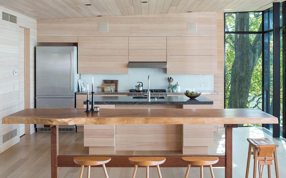 Cette photo montre une cuisine américaine parallèle montagne en bois clair avec une crédence blanche, parquet clair, îlot, un sol beige et un placard à porte plane.