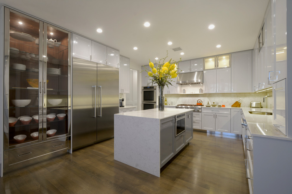Ejemplo de cocinas en L contemporánea con fregadero de un seno, armarios estilo shaker, puertas de armario blancas, salpicadero blanco, electrodomésticos de acero inoxidable, suelo de madera en tonos medios y una isla