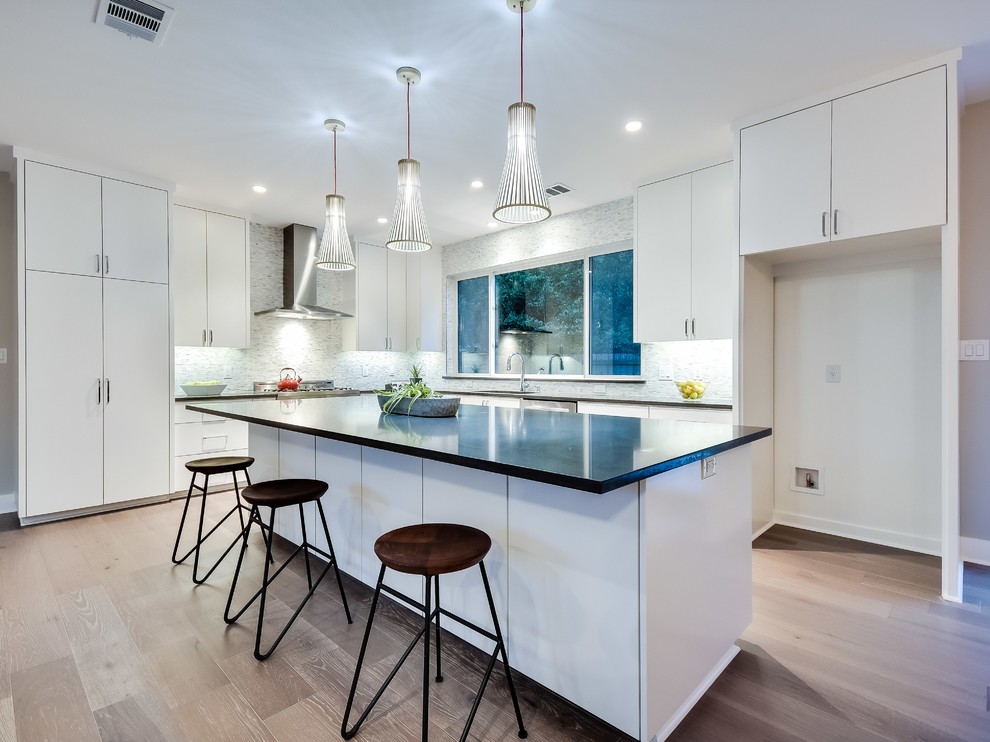Large trendy l-shaped light wood floor open concept kitchen photo in Austin with an undermount sink, flat-panel cabinets, white cabinets, quartz countertops, gray backsplash, stone tile backsplash, stainless steel appliances and an island