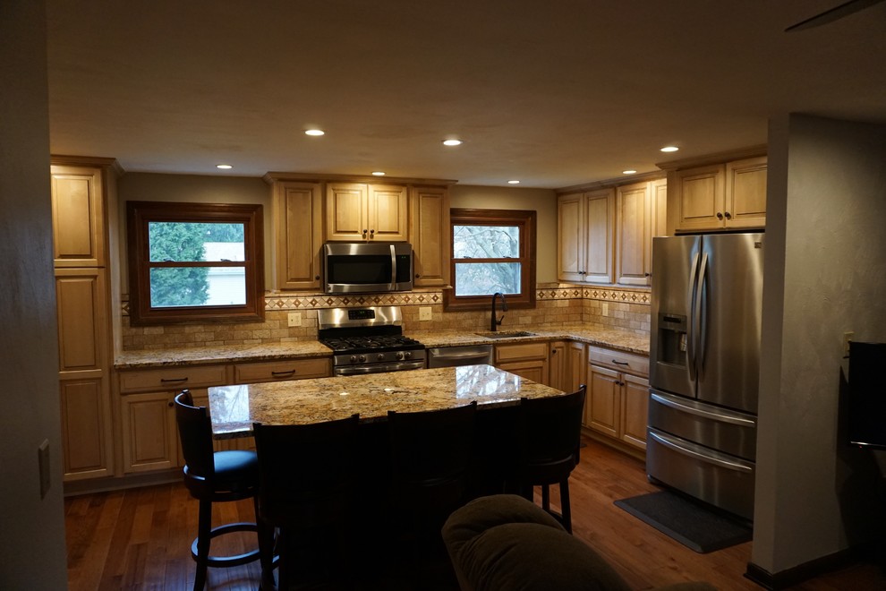 Inredning av ett klassiskt mellanstort kök, med en undermonterad diskho, luckor med upphöjd panel, skåp i ljust trä, granitbänkskiva, brunt stänkskydd, stänkskydd i travertin, rostfria vitvaror, mellanmörkt trägolv, en köksö och brunt golv