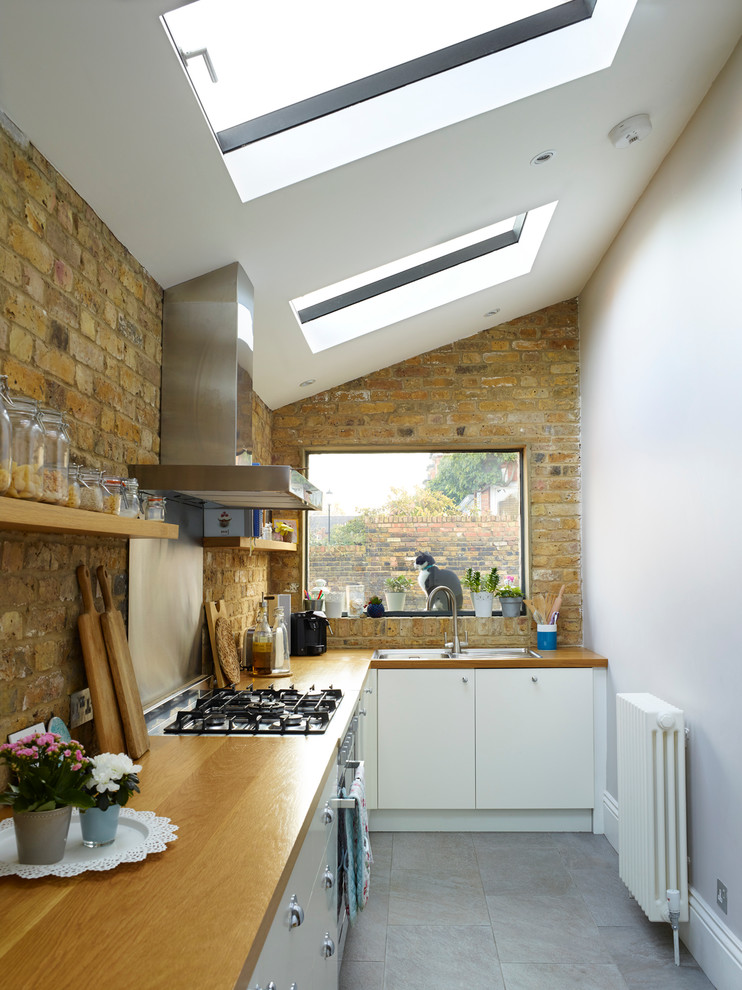 Design ideas for a contemporary l-shaped kitchen in London with a built-in sink, flat-panel cabinets, white cabinets, wood worktops, brick splashback and no island.