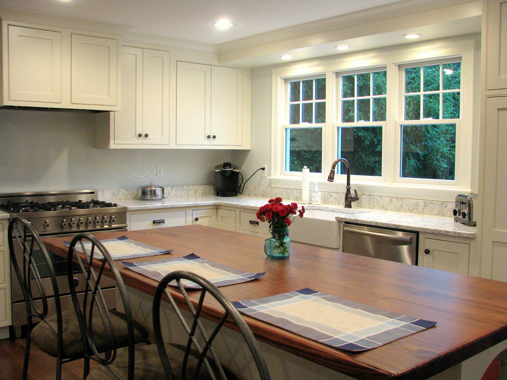 Klassisk inredning av ett mellanstort kök, med en rustik diskho, luckor med profilerade fronter, vita skåp, bänkskiva i kvarts, vitt stänkskydd, rostfria vitvaror, mörkt trägolv och en köksö