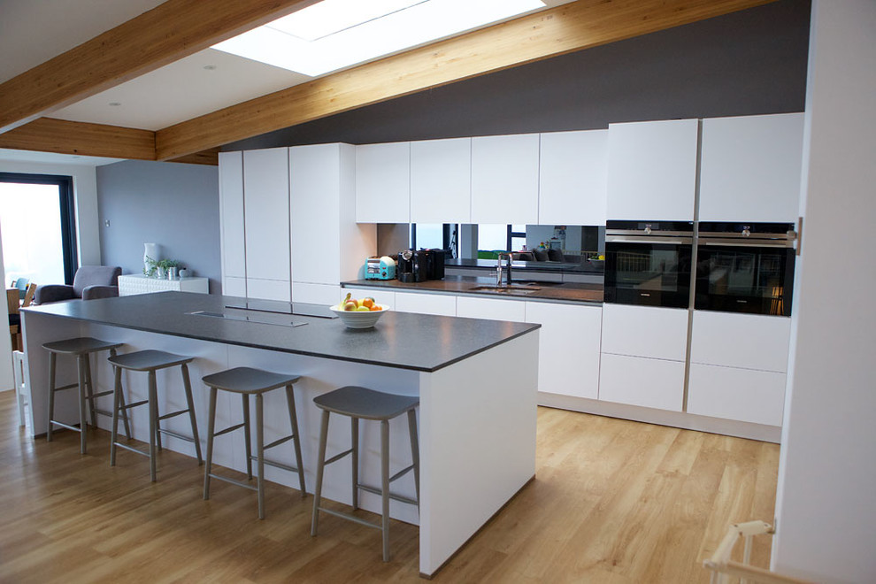 Идея дизайна: большая прямая кухня-гостиная в современном стиле с плоскими фасадами, белыми фасадами, зеркальным фартуком, техникой под мебельный фасад и полуостровом