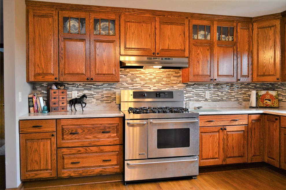 Example of a large mountain style u-shaped medium tone wood floor and brown floor enclosed kitchen design in Other with an undermount sink, raised-panel cabinets, medium tone wood cabinets, solid surface countertops, multicolored backsplash, matchstick tile backsplash, stainless steel appliances, no island and beige countertops