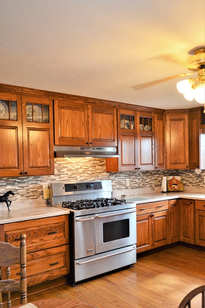 Example of a large mountain style u-shaped medium tone wood floor and brown floor enclosed kitchen design in Other with an undermount sink, raised-panel cabinets, medium tone wood cabinets, solid surface countertops, multicolored backsplash, matchstick tile backsplash, stainless steel appliances, no island and beige countertops