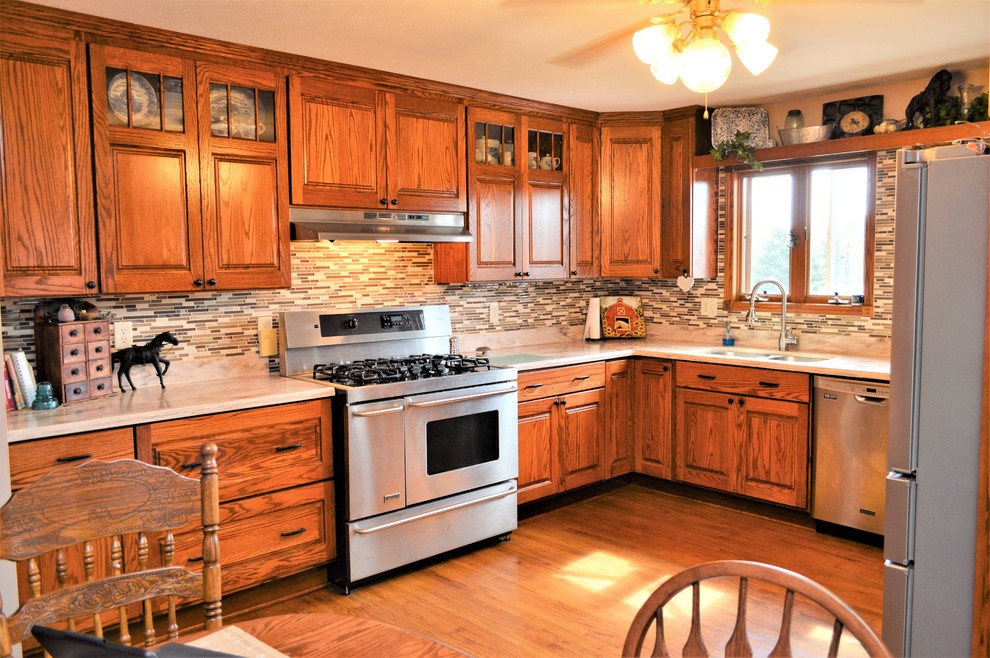Large mountain style u-shaped medium tone wood floor and brown floor enclosed kitchen photo in Other with an undermount sink, raised-panel cabinets, medium tone wood cabinets, solid surface countertops, multicolored backsplash, matchstick tile backsplash, stainless steel appliances, no island and beige countertops