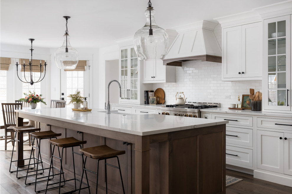 Idée de décoration pour une grande cuisine ouverte champêtre avec un évier de ferme, un placard à porte shaker, des portes de placard blanches, un plan de travail en quartz modifié, une crédence blanche, fenêtre, un électroménager en acier inoxydable, un sol en bois brun, îlot, un sol marron et un plan de travail blanc.