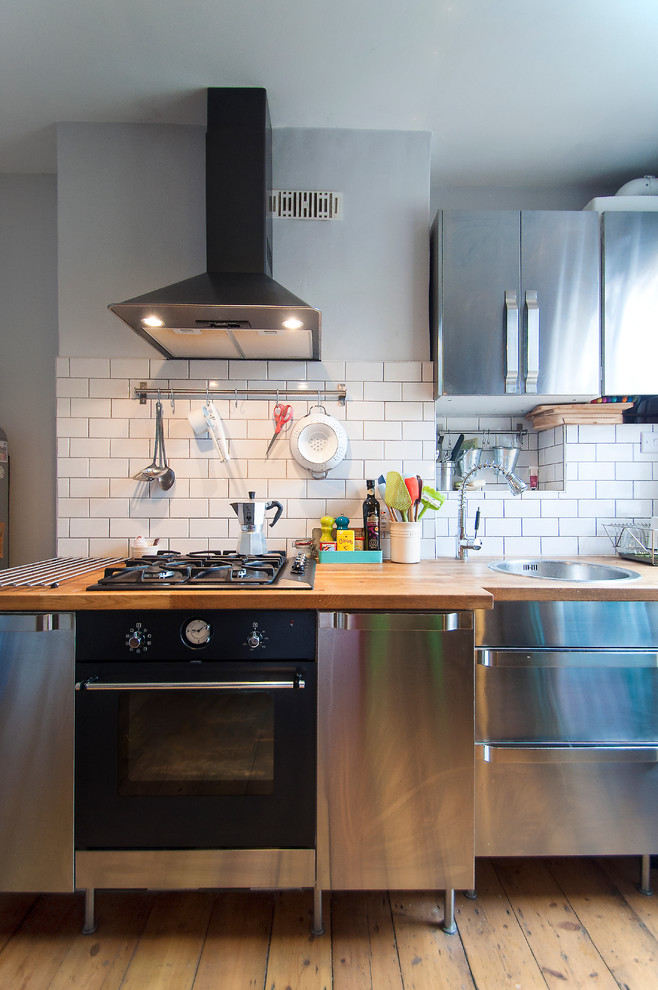 На фото: кухня в стиле фьюжн с фасадами из нержавеющей стали, накладной мойкой, плоскими фасадами и деревянной столешницей