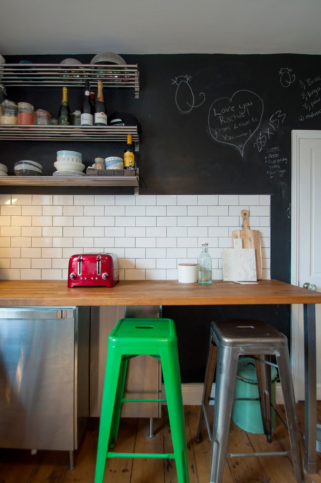 ロンドンにあるエクレクティックスタイルのおしゃれなカフェ風キッチン (フラットパネル扉のキャビネット、ステンレスキャビネット、木材カウンター、白いキッチンパネル、サブウェイタイルのキッチンパネル、無垢フローリング) の写真