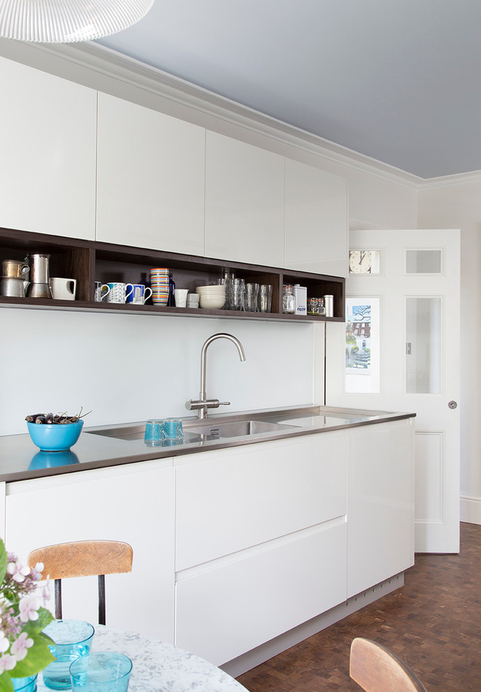Inspiration for a medium sized contemporary galley kitchen/diner in London with glass-front cabinets, grey cabinets, stainless steel worktops, no island, an integrated sink, stainless steel appliances and brown floors.