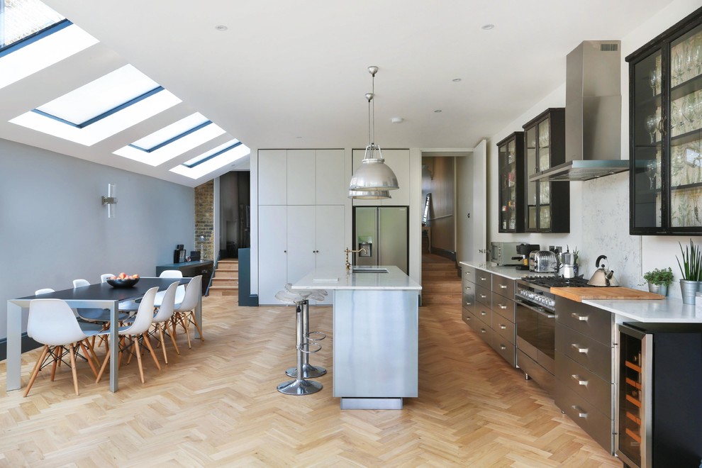 Modern inredning av ett stort linjärt kök och matrum, med en dubbel diskho, släta luckor, skåp i rostfritt stål, marmorbänkskiva, vitt stänkskydd, stänkskydd i marmor, rostfria vitvaror, ljust trägolv, en halv köksö och beiget golv