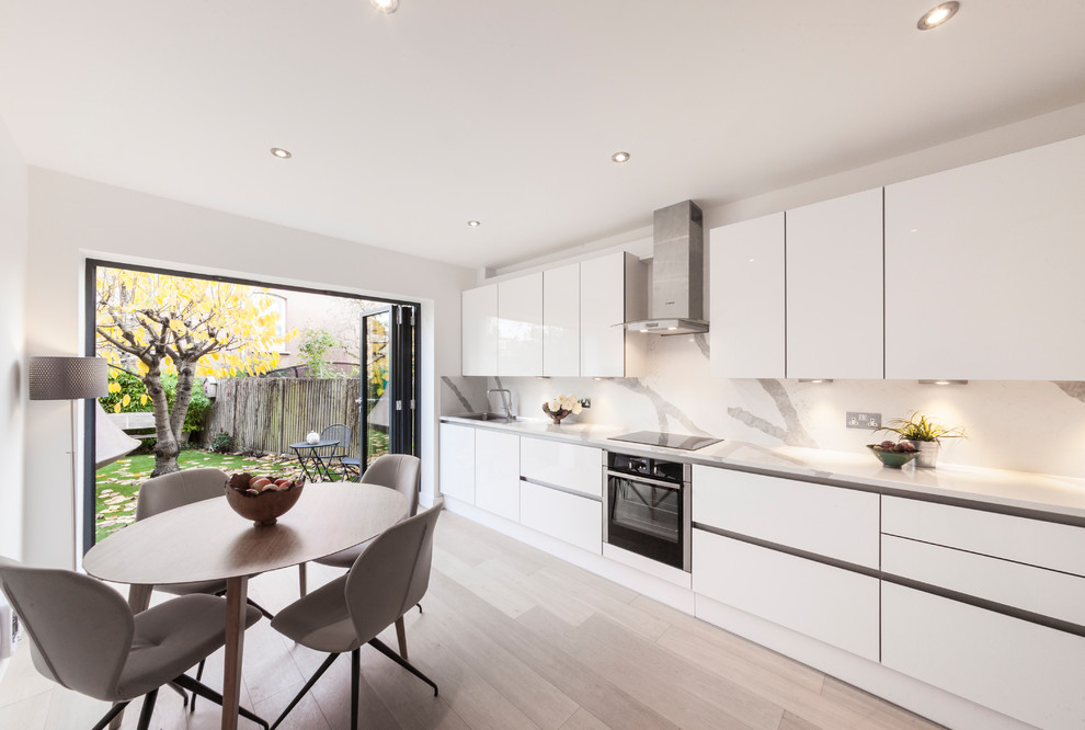 Einzeilige Moderne Wohnküche ohne Insel mit flächenbündigen Schrankfronten, weißen Schränken, Küchengeräten aus Edelstahl und weißer Arbeitsplatte in London