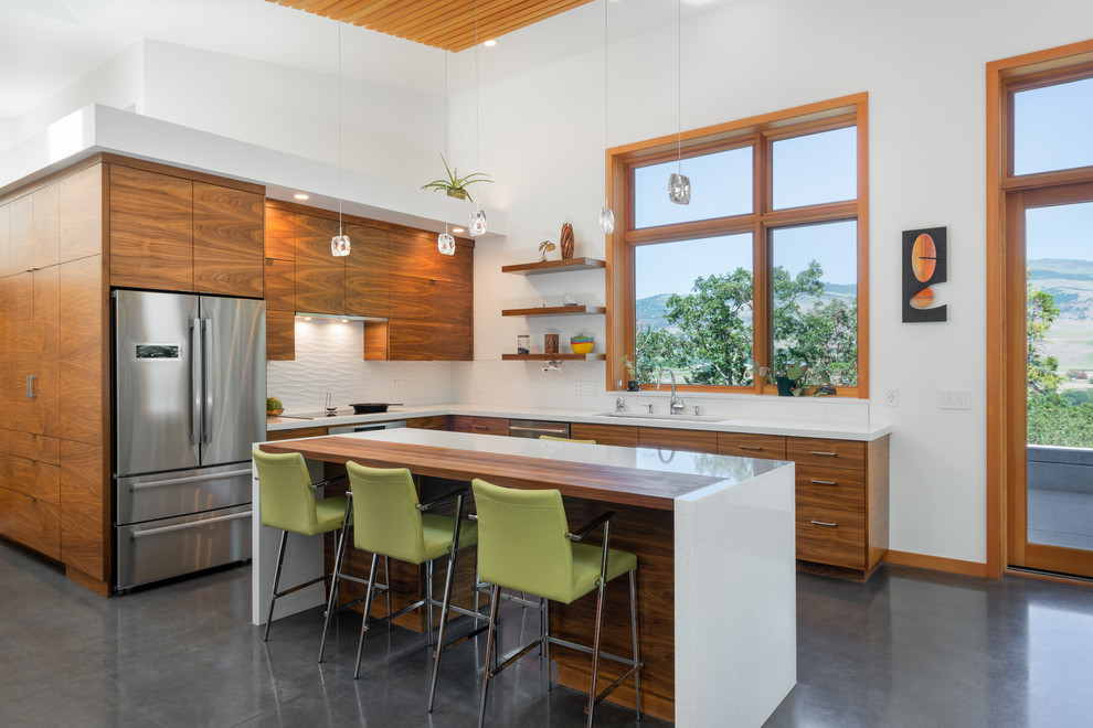 Example of a mid-sized trendy l-shaped concrete floor and gray floor eat-in kitchen design in Other with an undermount sink, medium tone wood cabinets, white backsplash, stainless steel appliances, an island, white countertops, flat-panel cabinets and ceramic backsplash