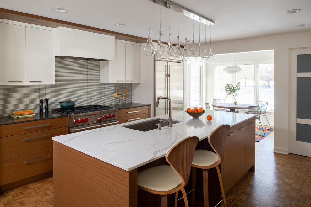 Foto på ett mellanstort retro vit kök, med en enkel diskho, släta luckor, skåp i mellenmörkt trä, bänkskiva i kvarts, vitt stänkskydd, rostfria vitvaror, mellanmörkt trägolv, en köksö och brunt golv