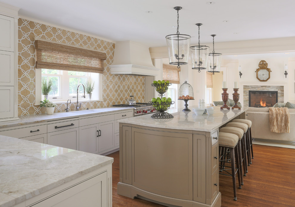 Klassisk inredning av ett kök, med en enkel diskho, luckor med profilerade fronter, vita skåp, flerfärgad stänkskydd, rostfria vitvaror, mellanmörkt trägolv och en köksö