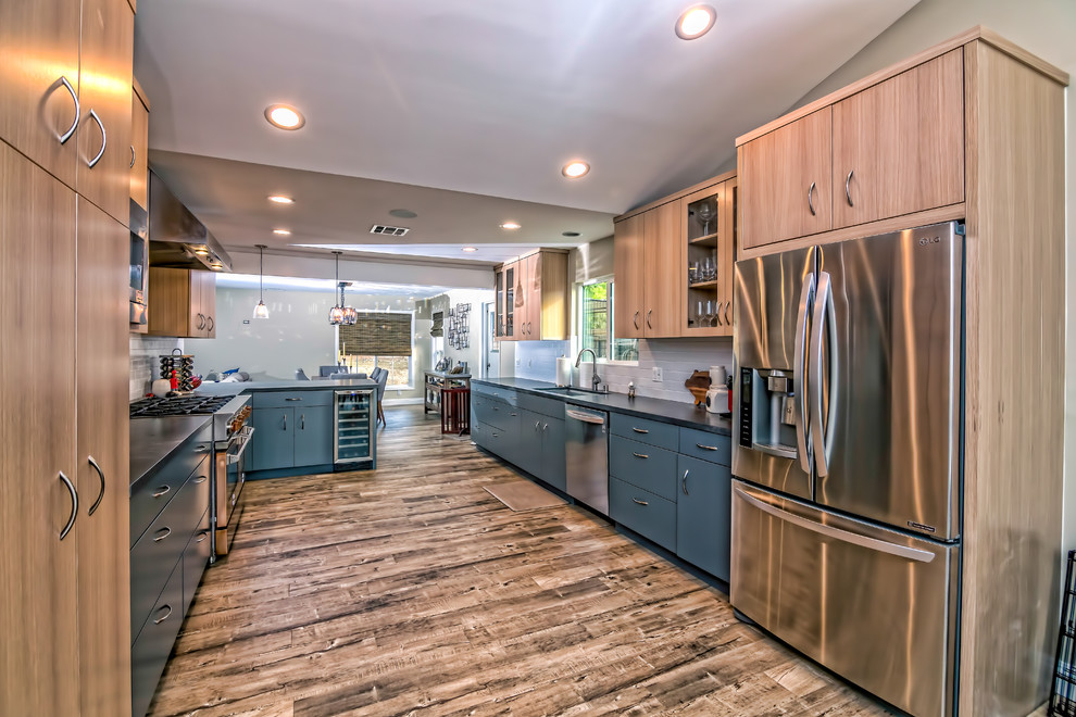 Photo of a large traditional u-shaped kitchen/diner in San Francisco with a submerged sink, flat-panel cabinets, metro tiled splashback, stainless steel appliances, white splashback, medium hardwood flooring, a breakfast bar and blue cabinets.