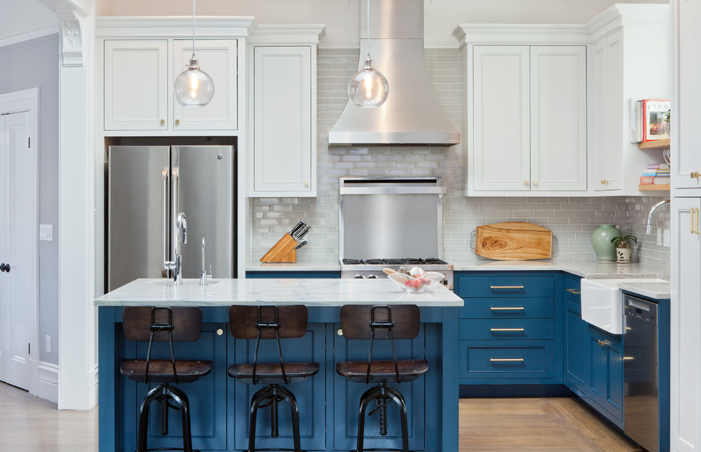 This is an example of a traditional l-shaped kitchen in San Francisco with a belfast sink, shaker cabinets, blue cabinets, grey splashback, metro tiled splashback, stainless steel appliances, light hardwood flooring, an island and white worktops.