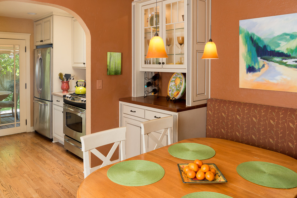 Amerikansk inredning av ett litet kök, med mellanmörkt trägolv, en dubbel diskho, luckor med upphöjd panel, beige skåp, bänkskiva i kvarts, orange stänkskydd, stänkskydd i keramik och rostfria vitvaror