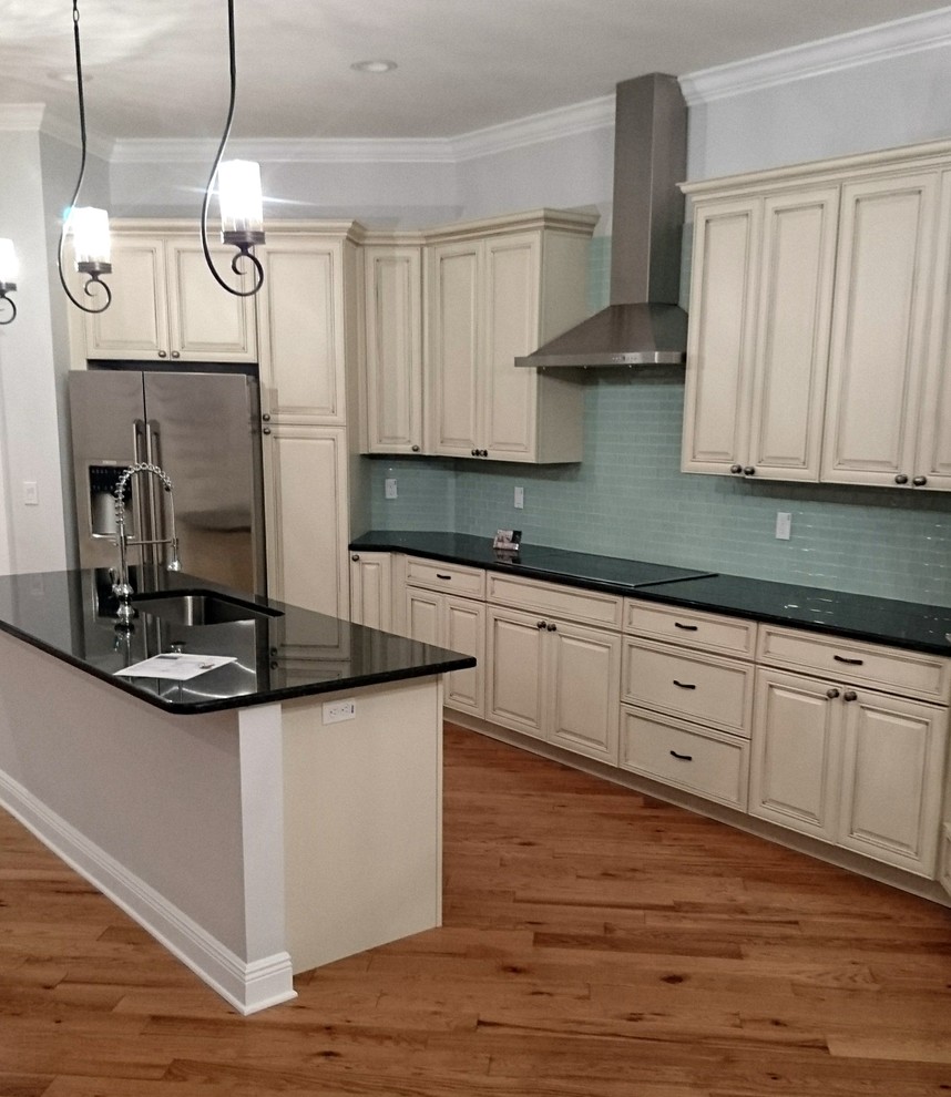 Mid-sized elegant single-wall medium tone wood floor open concept kitchen photo in Tampa with an undermount sink, raised-panel cabinets, white cabinets, granite countertops, blue backsplash, ceramic backsplash, stainless steel appliances and an island