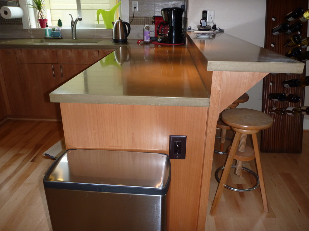 Photo of a small classic u-shaped kitchen/diner in Portland with a double-bowl sink, flat-panel cabinets, light wood cabinets, concrete worktops, stainless steel appliances, light hardwood flooring and a breakfast bar.
