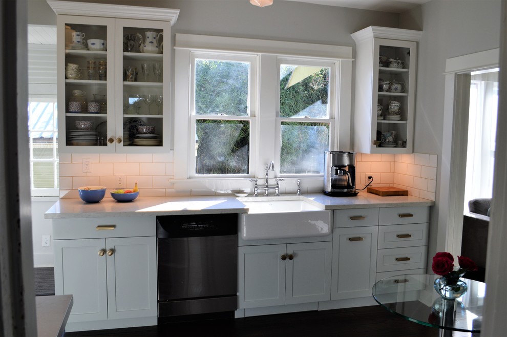 Idéer för små amerikanska u-kök, med en rustik diskho, skåp i shakerstil, vita skåp, marmorbänkskiva, vitt stänkskydd, stänkskydd i porslinskakel, rostfria vitvaror, mörkt trägolv och brunt golv