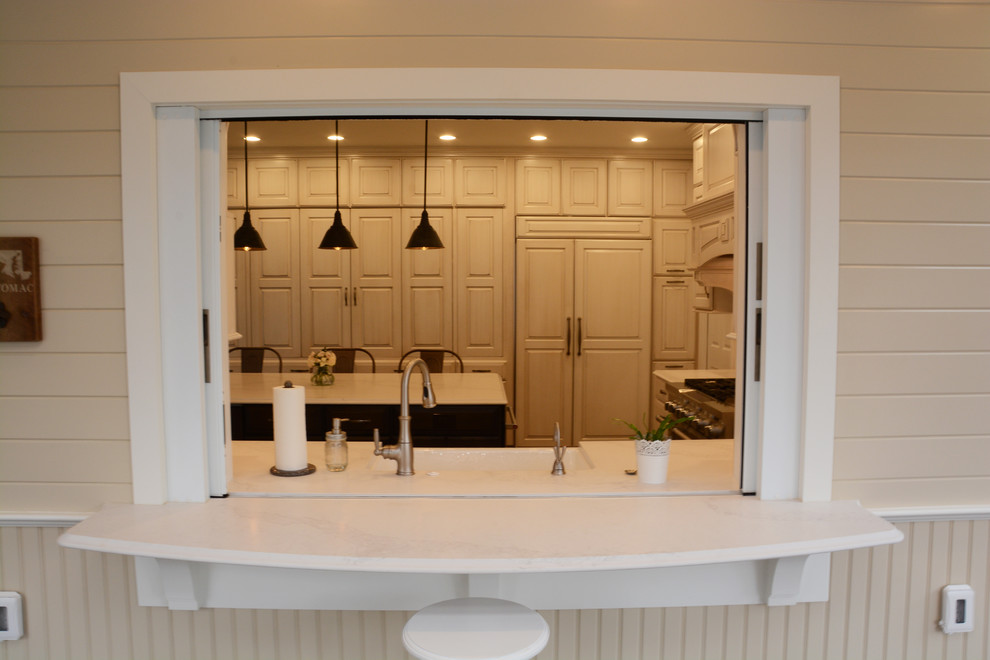Klassisk inredning av ett stort kök, med en rustik diskho, luckor med upphöjd panel, vita skåp, bänkskiva i kvarts, vitt stänkskydd, rostfria vitvaror, mörkt trägolv, en köksö och brunt golv