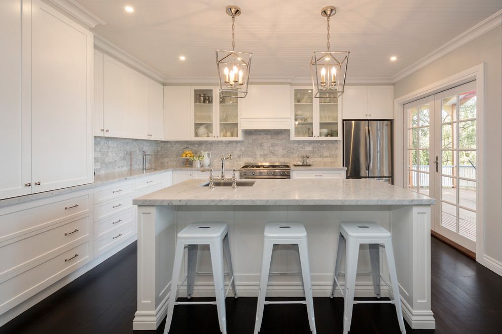 Photo of a classic l-shaped kitchen in Melbourne with a submerged sink, shaker cabinets, white cabinets, grey splashback, stainless steel appliances, dark hardwood flooring, an island, brown floors and white worktops.