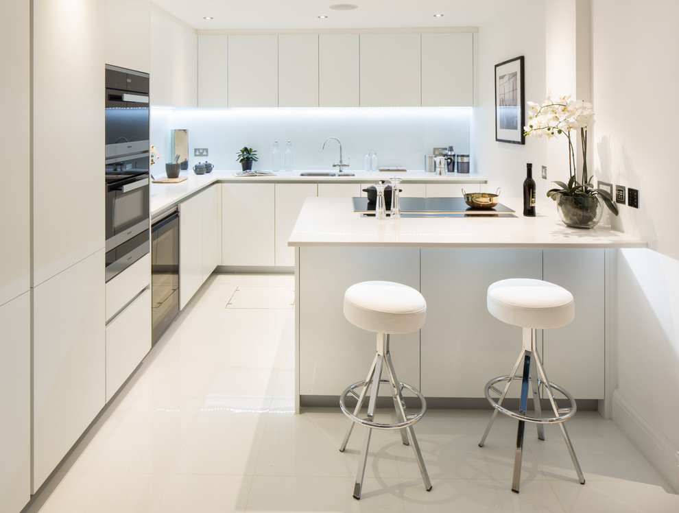 Moderne Küche in L-Form mit Unterbauwaschbecken, flächenbündigen Schrankfronten, weißen Schränken, Küchenrückwand in Blau, Küchengeräten aus Edelstahl und Kücheninsel in London