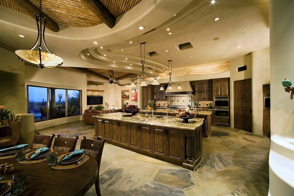 Inspiration for a large southwestern single-wall concrete floor and multicolored floor open concept kitchen remodel in Phoenix with an undermount sink, raised-panel cabinets, dark wood cabinets, granite countertops, beige backsplash, travertine backsplash, stainless steel appliances and two islands