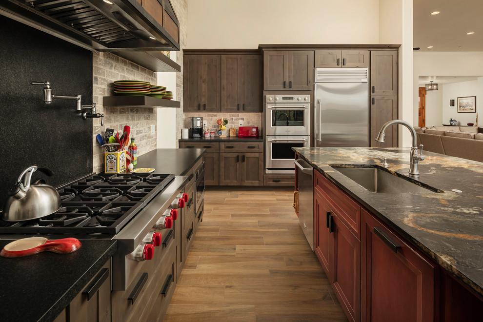 フェニックスにある高級な広いサンタフェスタイルのおしゃれなキッチン (アンダーカウンターシンク、レイズドパネル扉のキャビネット、茶色いキャビネット、御影石カウンター、茶色いキッチンパネル、レンガのキッチンパネル、シルバーの調理設備、セラミックタイルの床、茶色い床、茶色いキッチンカウンター、壁紙) の写真