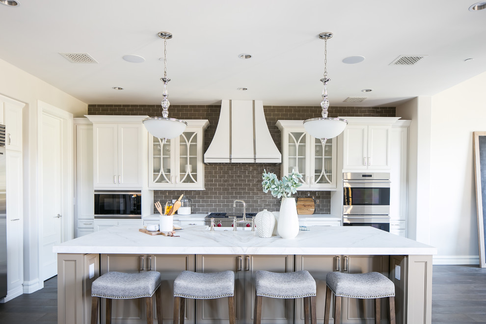 Zweizeilige Klassische Küche mit Kassettenfronten, weißen Schränken, Küchenrückwand in Grau, Küchengeräten aus Edelstahl, dunklem Holzboden, Kücheninsel und braunem Boden in Phoenix