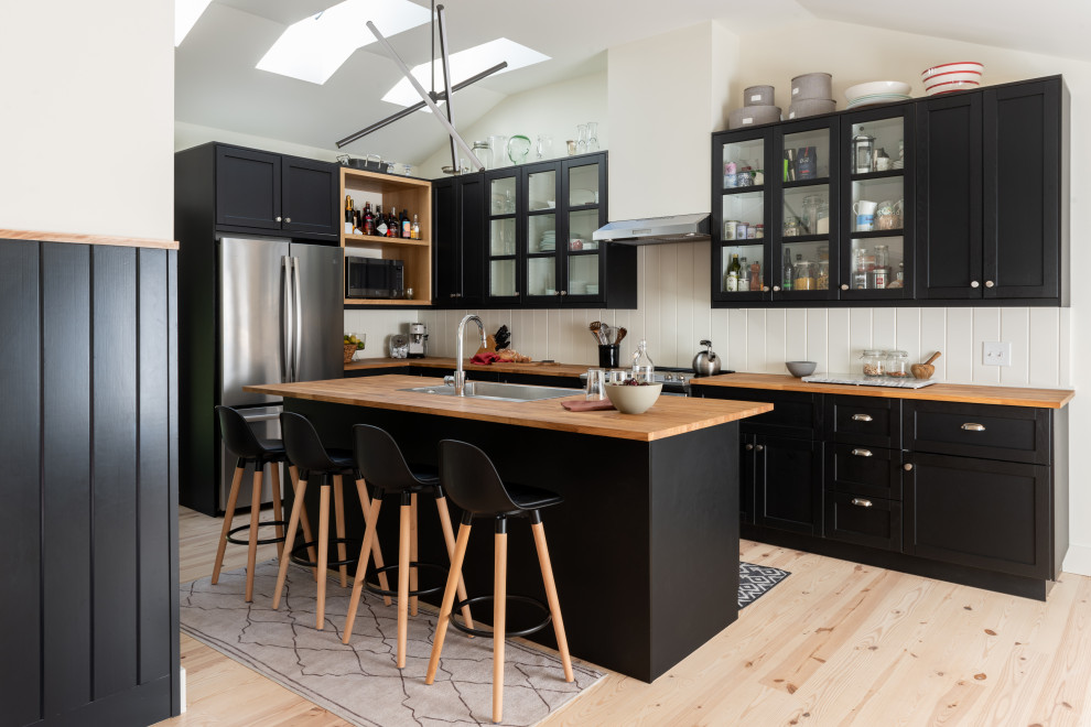 Idéer för ett modernt brun l-kök, med en undermonterad diskho, skåp i shakerstil, svarta skåp, träbänkskiva, rostfria vitvaror, ljust trägolv, en köksö och beiget golv