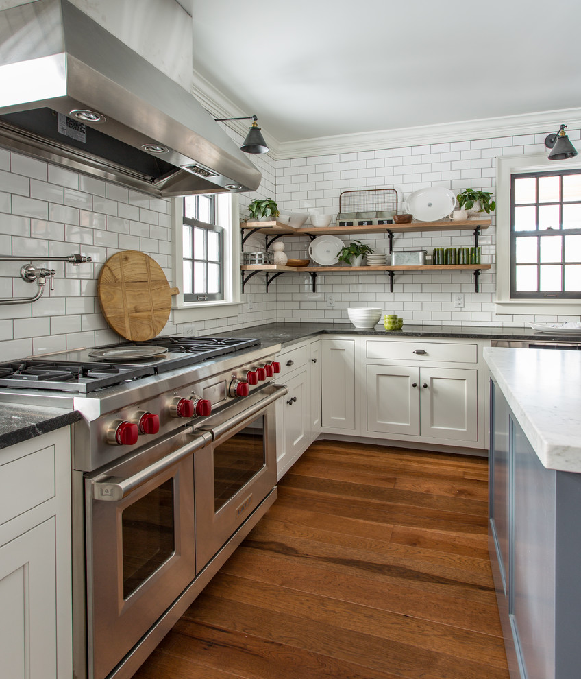 Lantlig inredning av ett kök, med luckor med infälld panel, vita skåp, stänkskydd i tunnelbanekakel, rostfria vitvaror, mellanmörkt trägolv och en köksö