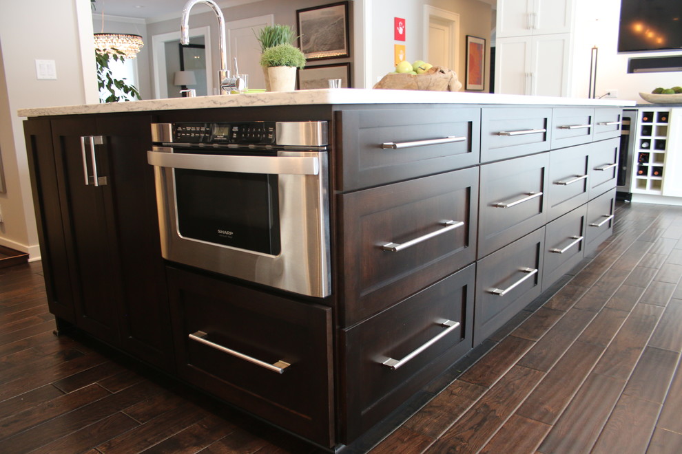 Example of a mid-sized trendy l-shaped dark wood floor and brown floor eat-in kitchen design in Milwaukee with a farmhouse sink, shaker cabinets, dark wood cabinets, quartz countertops, white backsplash, subway tile backsplash, stainless steel appliances, an island and white countertops