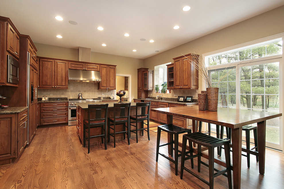 Eat-in kitchen - traditional u-shaped eat-in kitchen idea in Chicago with raised-panel cabinets, medium tone wood cabinets, beige backsplash and paneled appliances