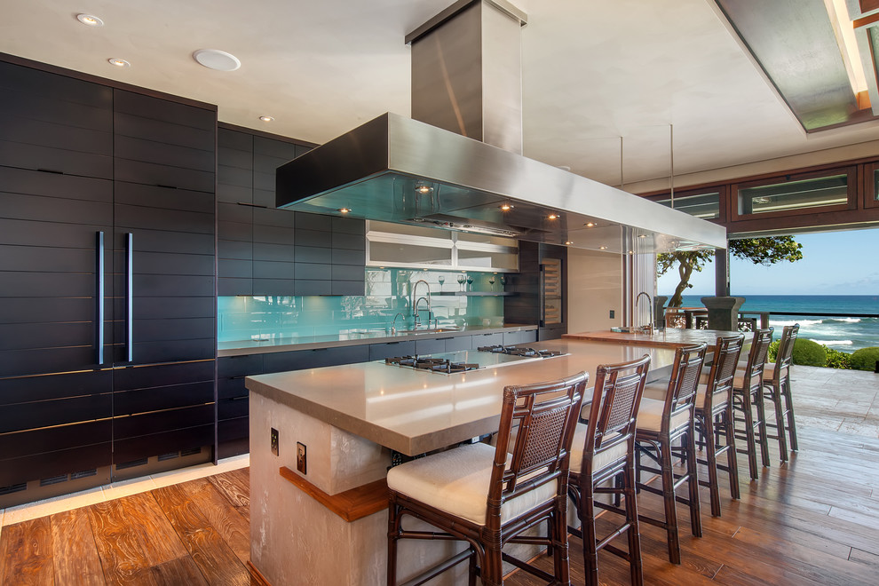 Küche mit schwarzen Schränken, Küchenrückwand in Grün, braunem Holzboden, Kücheninsel und grauer Arbeitsplatte in Hawaii