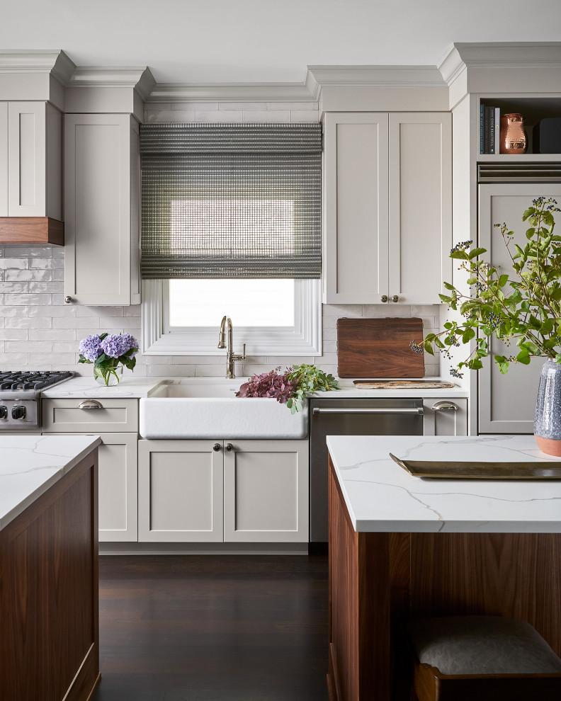 Inspiration for a transitional dark wood floor kitchen remodel in Chicago with a farmhouse sink, shaker cabinets, beige cabinets, white backsplash, stainless steel appliances, two islands and white countertops