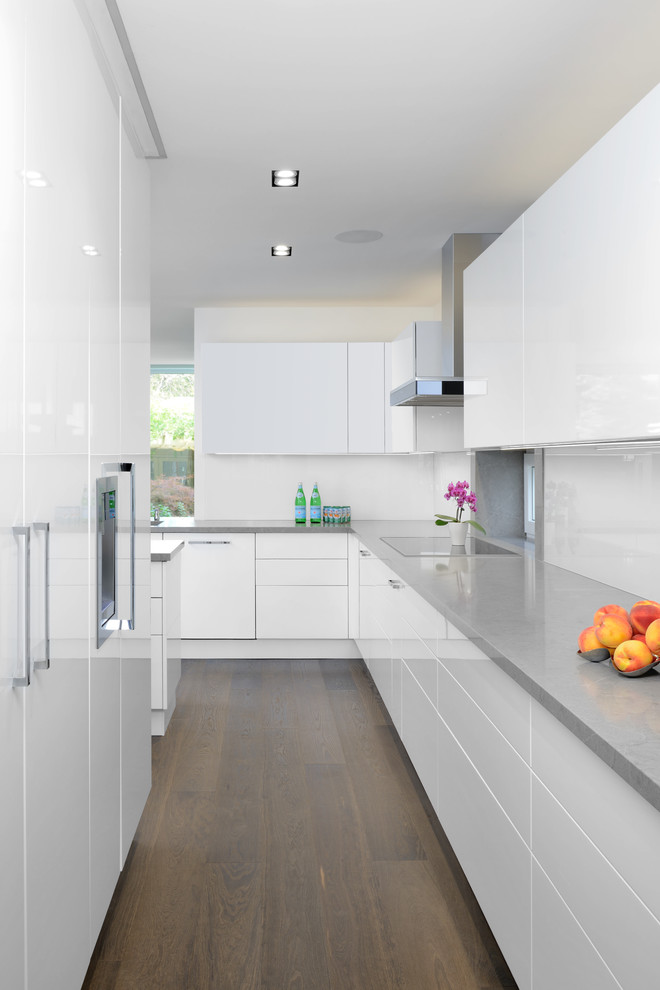 This is an example of a contemporary kitchen in Toronto with flat-panel cabinets, white cabinets, white splashback, glass sheet splashback, integrated appliances and dark hardwood flooring.
