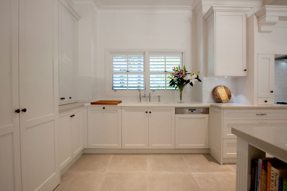 Expansive classic u-shaped open plan kitchen in Sydney with a submerged sink, shaker cabinets, white cabinets, engineered stone countertops, white splashback, metro tiled splashback, stainless steel appliances, ceramic flooring and an island.
